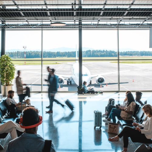 Diverse people sitting and standing at departures terminal. Each killing time their own way while waiting for their flight.