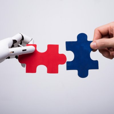 Close-up Of Robot And Human Hand Holding Red And Blue Jigsaw Puzzle